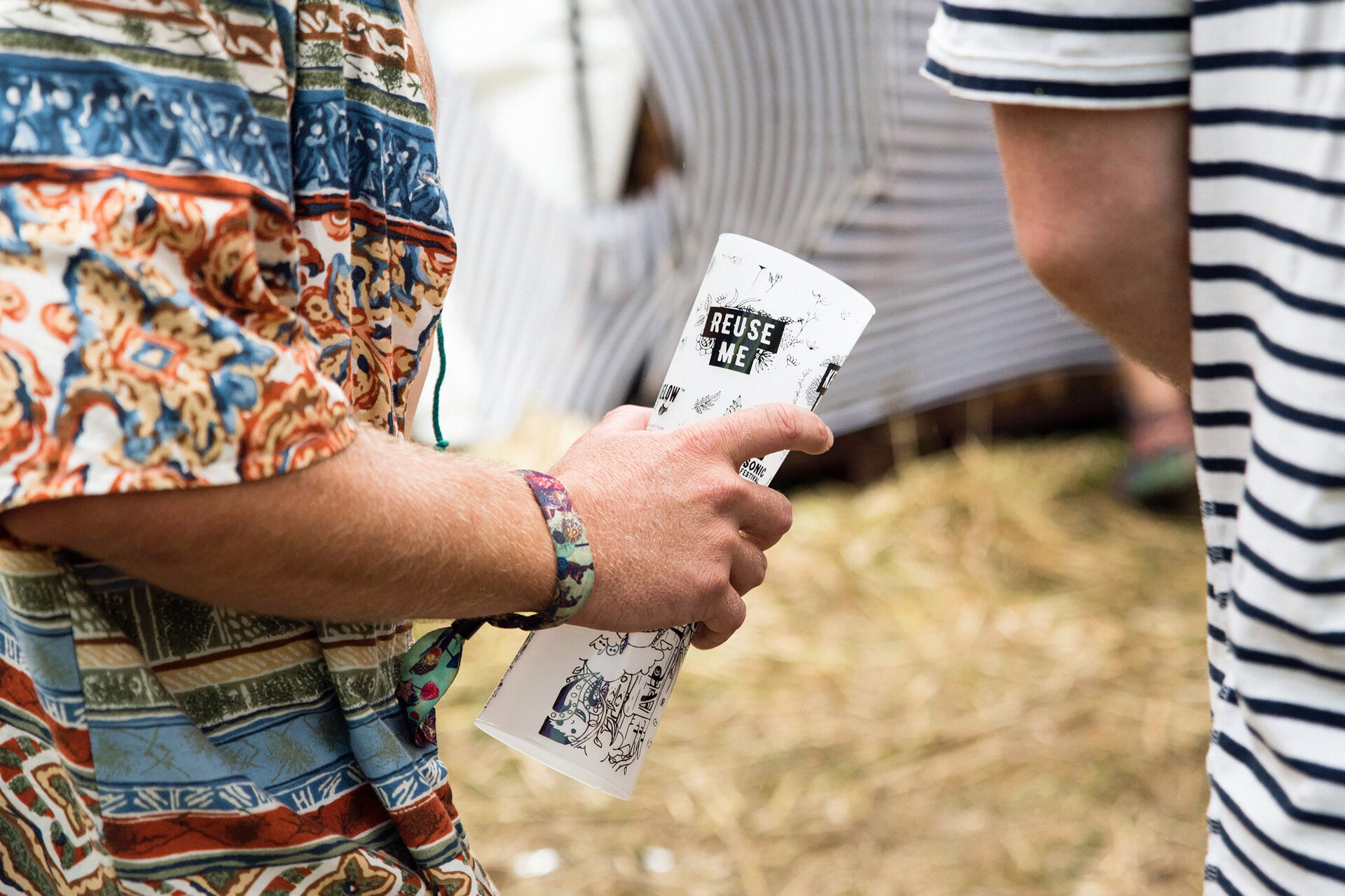 Nahaufnahme. Zwei Männer von hinten auf einem Festival. Der eine Mann hält zwei Mehrwegbecher in der Hand.