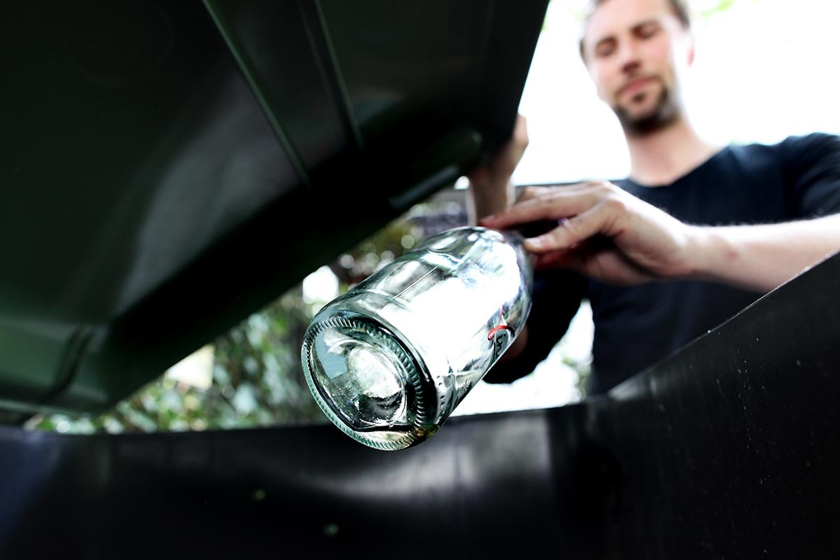 Ein Mann wirft eine leere Glasflasche in eine schwarze Tonne.