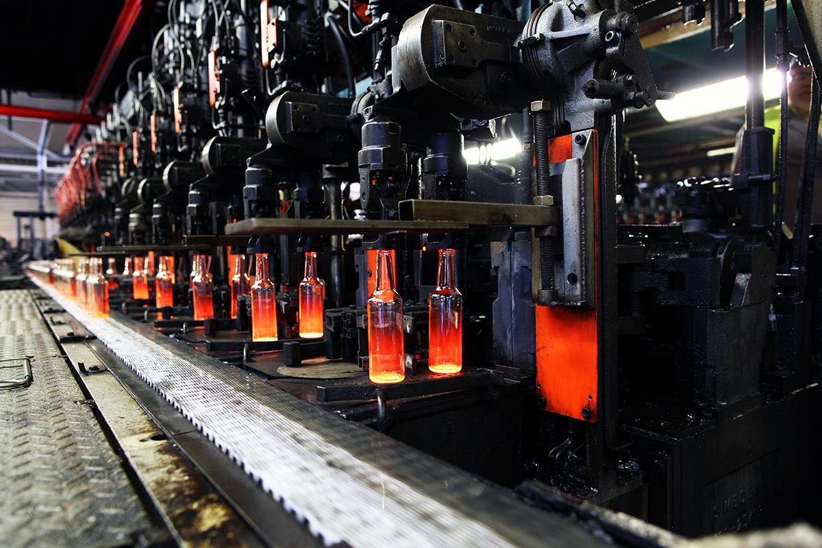 Glühende fertige Glasflaschen laufen aufgereiht nebeneinander aus einer Produktionsmaschine.