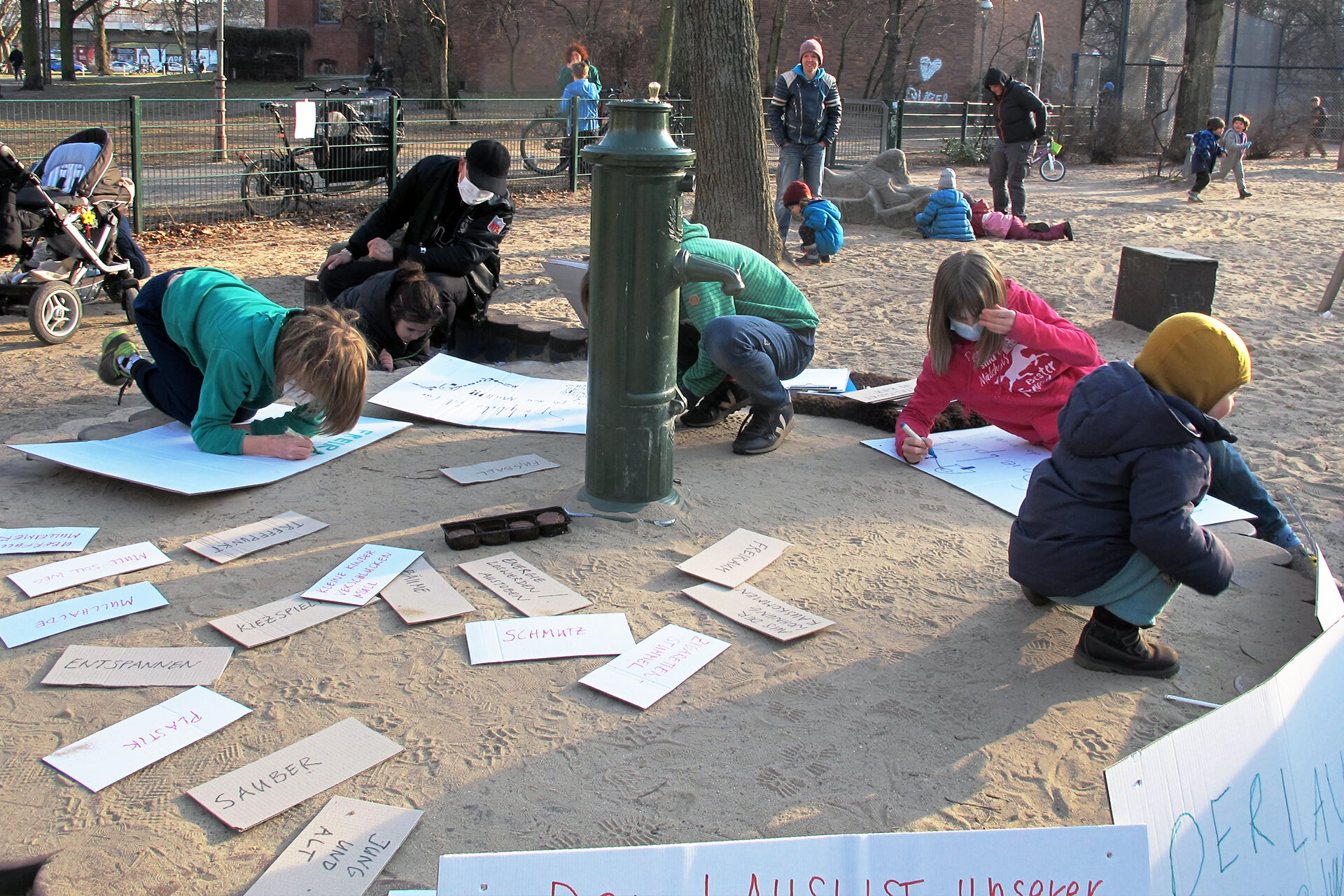Mehrere Kinder schreiben auf einem Spielplatz Plakate gegen Vermüllung