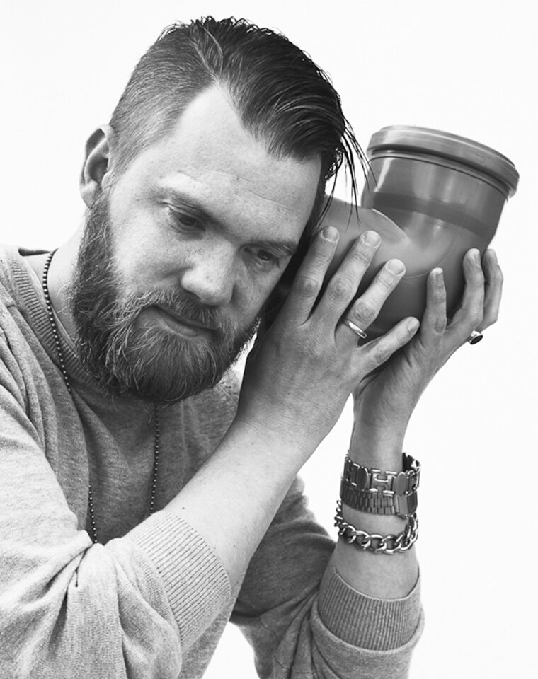 Mann mit Bart hält sich das Verbindungsstück eines Abflussrohrs an das linke Ohr und lauscht.