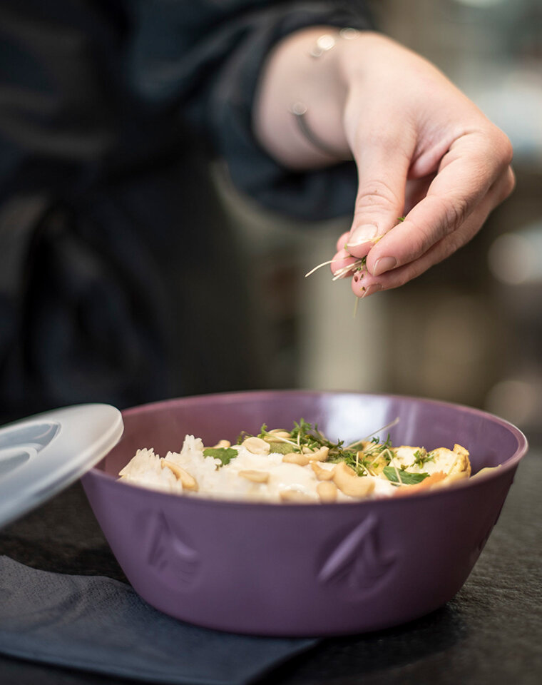 Schüssel mit Essen. Hand streut Kräuter in die Schüssel.