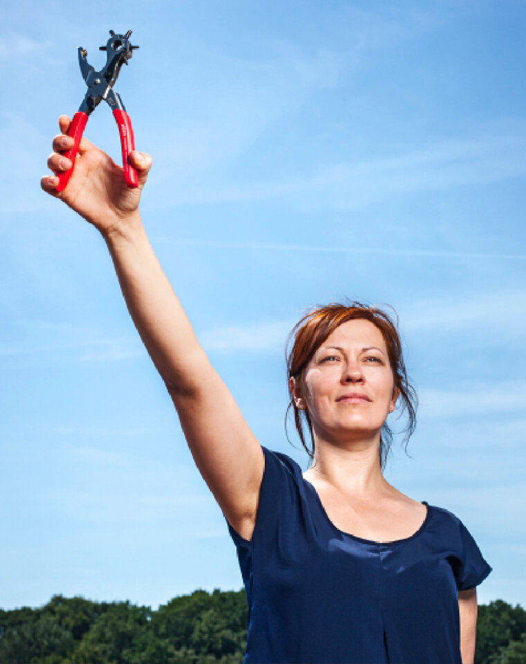Frau hält eine Zange in die Luft. Im Hintergrund blauer Himmel.
