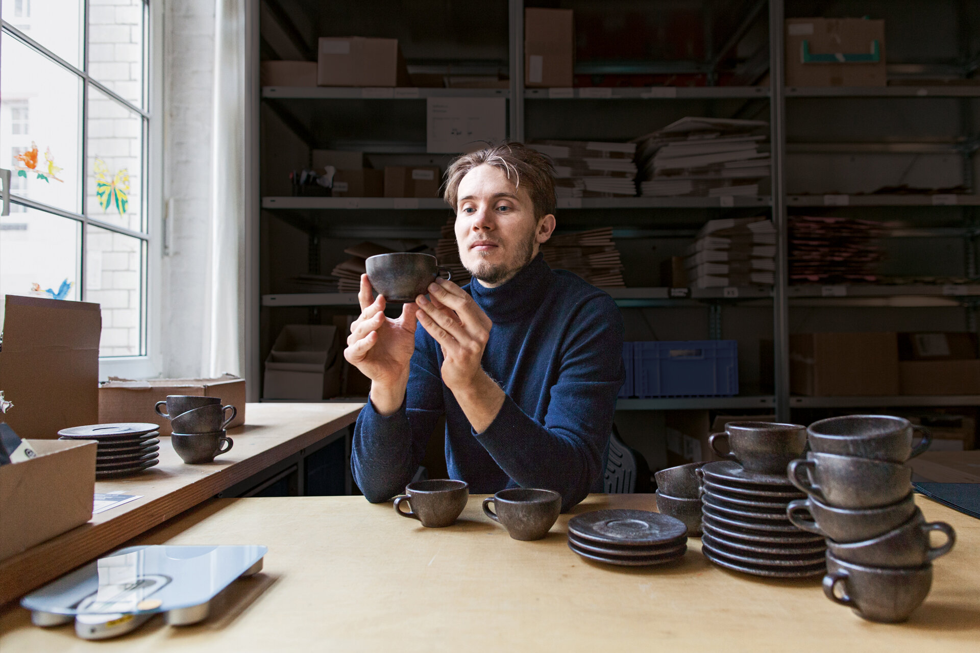 Mann sitztneben dem Fenster am Schreibtisch und begutachtet seine aus Kaffeesatz produzierte Kafeetasse