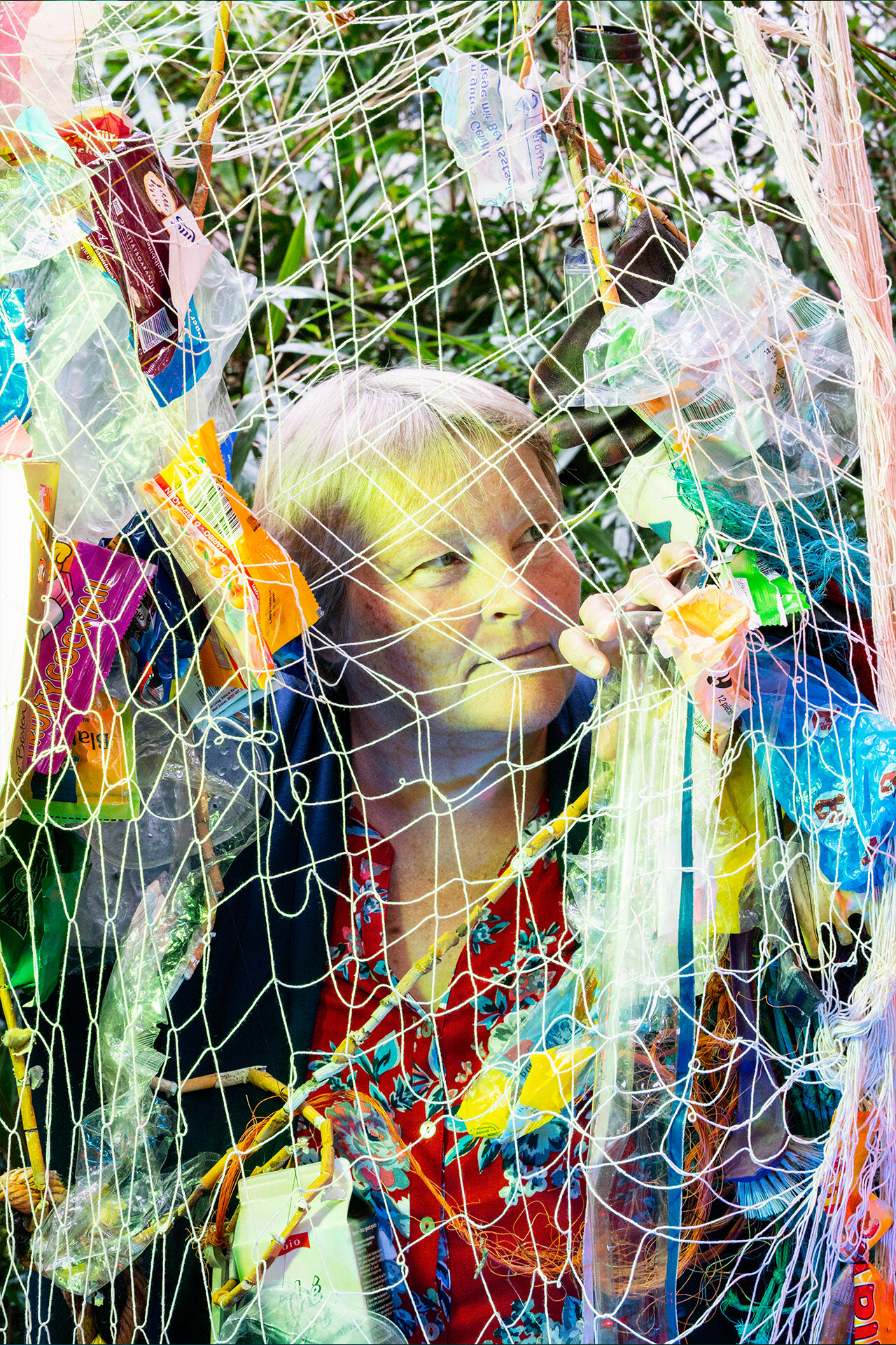Ältere Frau schaut durch ein mit Plastikmüll gespicktes Fischernetz.