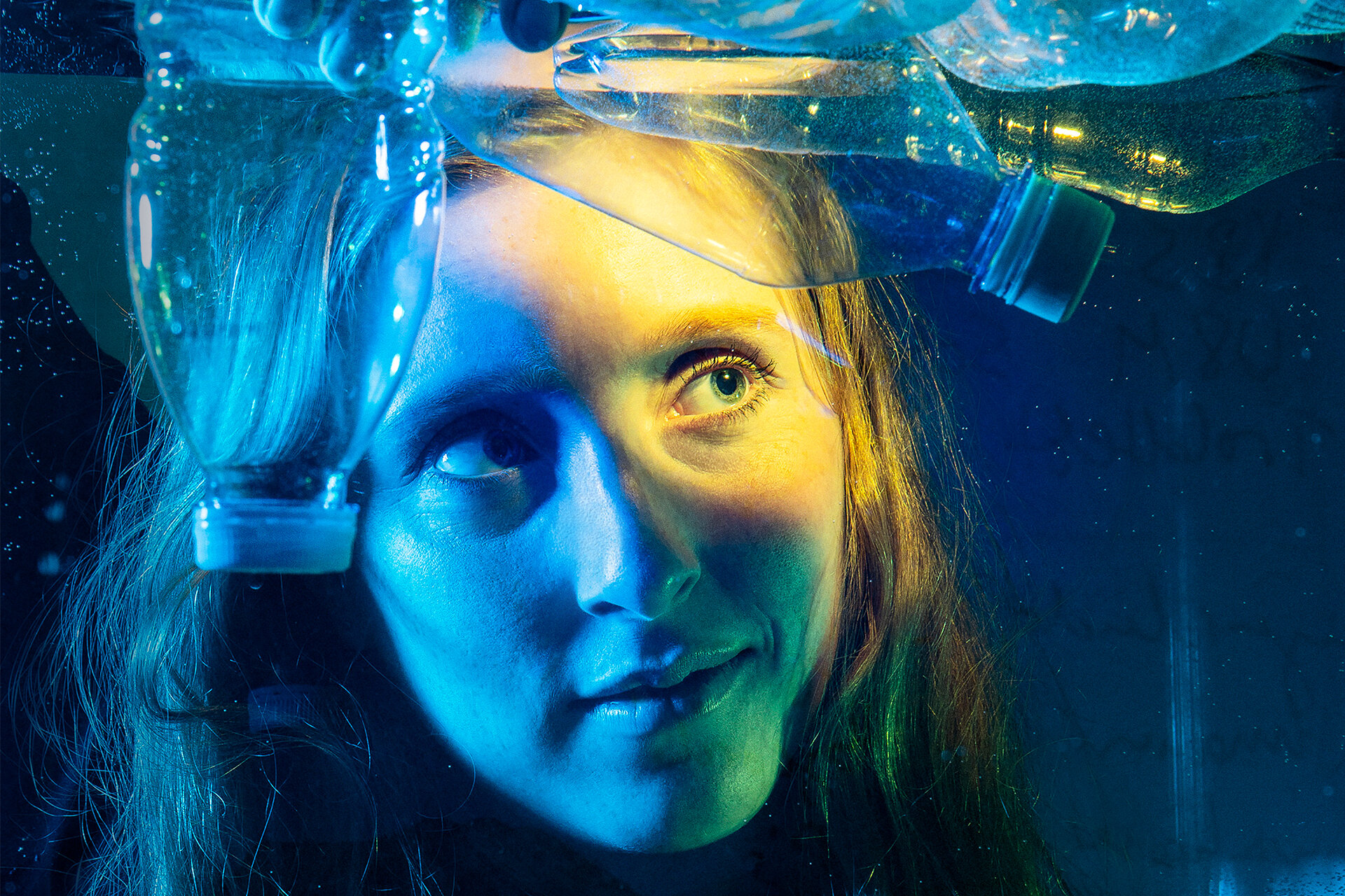Frau schaut in ein Glaswasserbecken mit leeren schwimmenden Plastikflaschen.