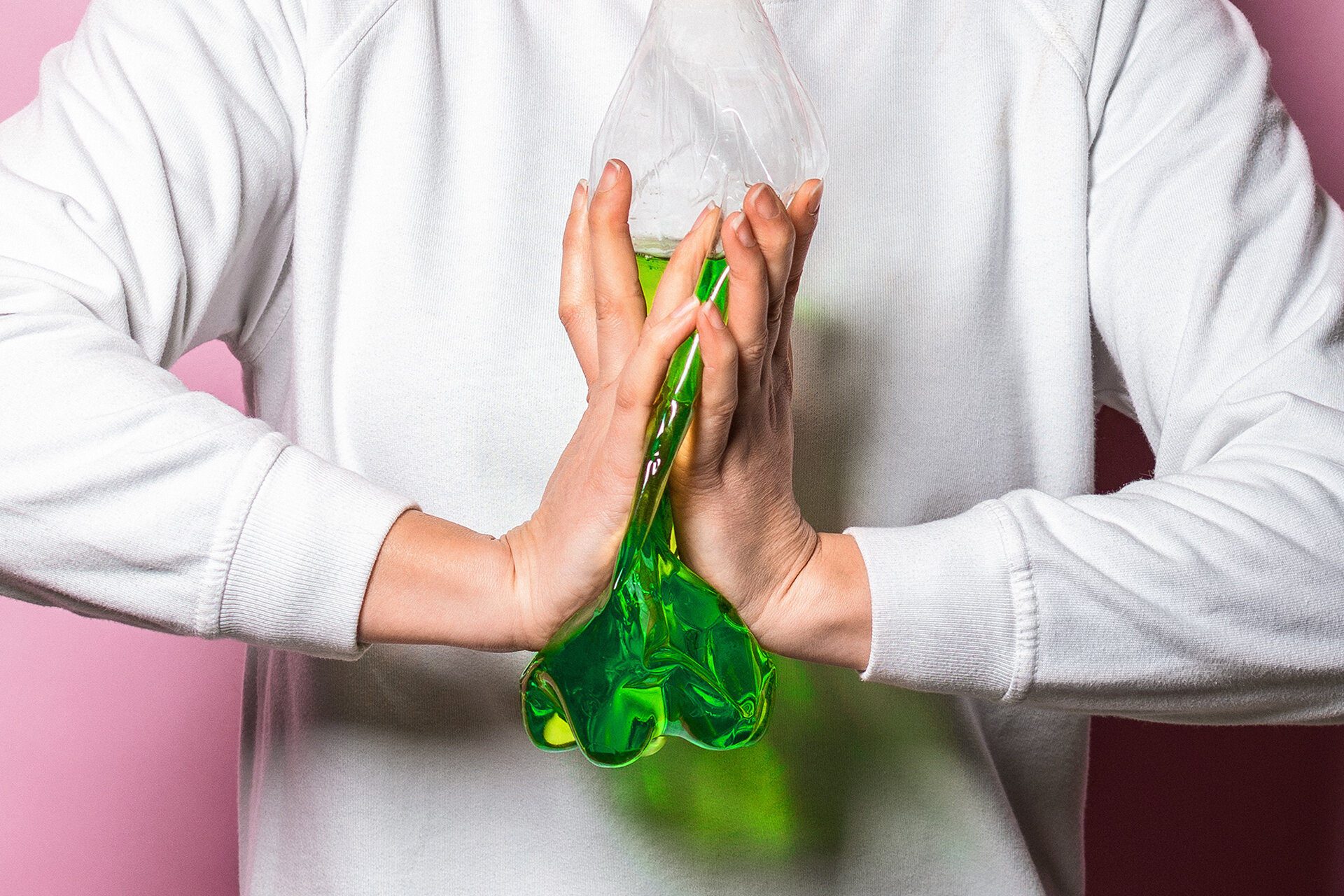 Person zerquetscht Plastikflasche mit einer grünen Flüssigkeit zwischen den Händen.