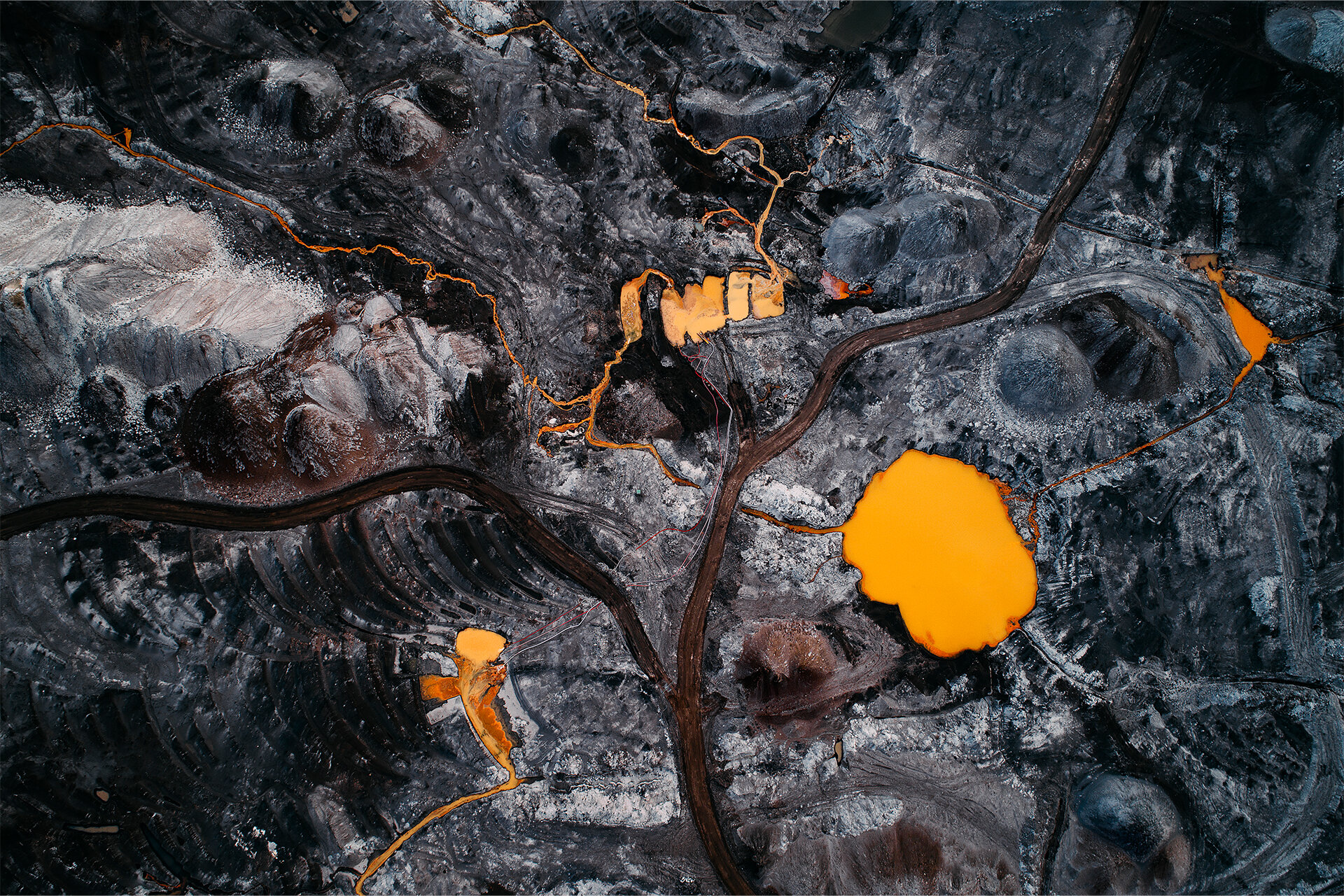 Luftaufnahme auf einen Braunkohleabbaugebiet. Ein schwarzes Feld druchzogen von Straßen und orange gefärbtem Wasser.