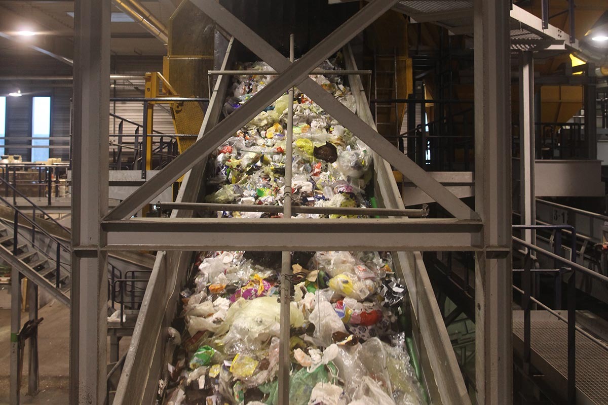 Plastikmüll wird auf einem Förderband durch eine Halle transportiert.