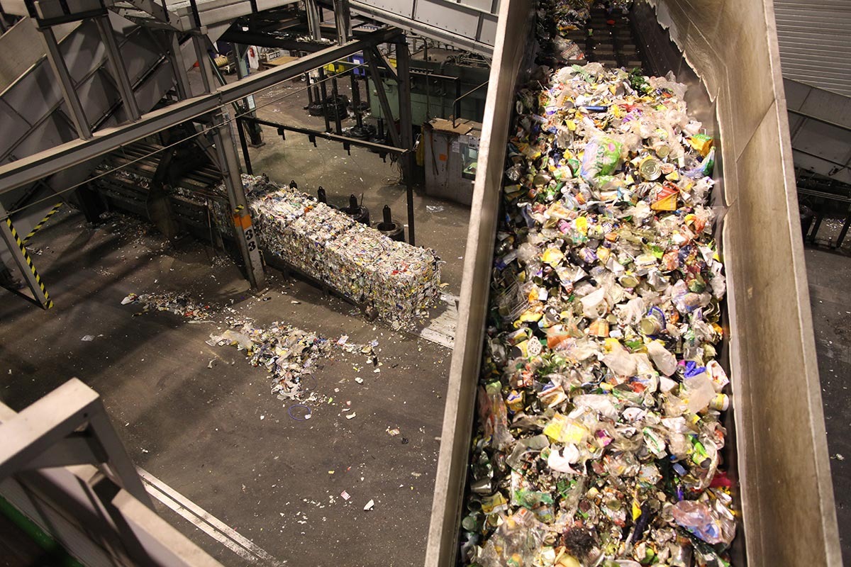 Blick von oben in eine Halle. Plastikmüll läuft über ein Förderband.