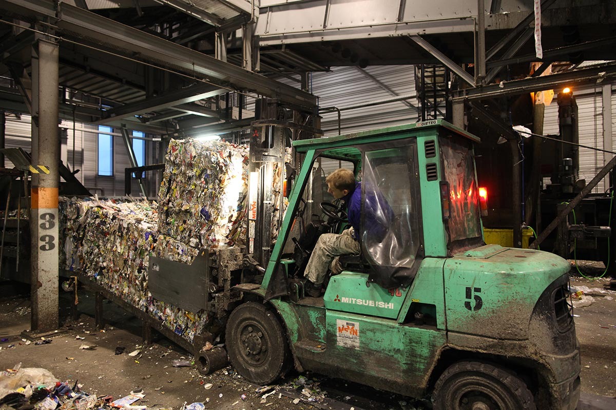 Ein Mann im Gabelstapler fährt gepressten Plastikmüll zum Ausgang einer Halle.