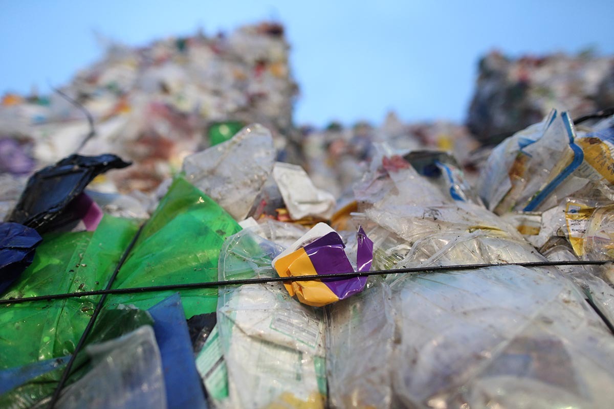 Ein Plastikjogurtbecher klemmt auf einem großen Plastikmüllballen mit einer Schnur fest.