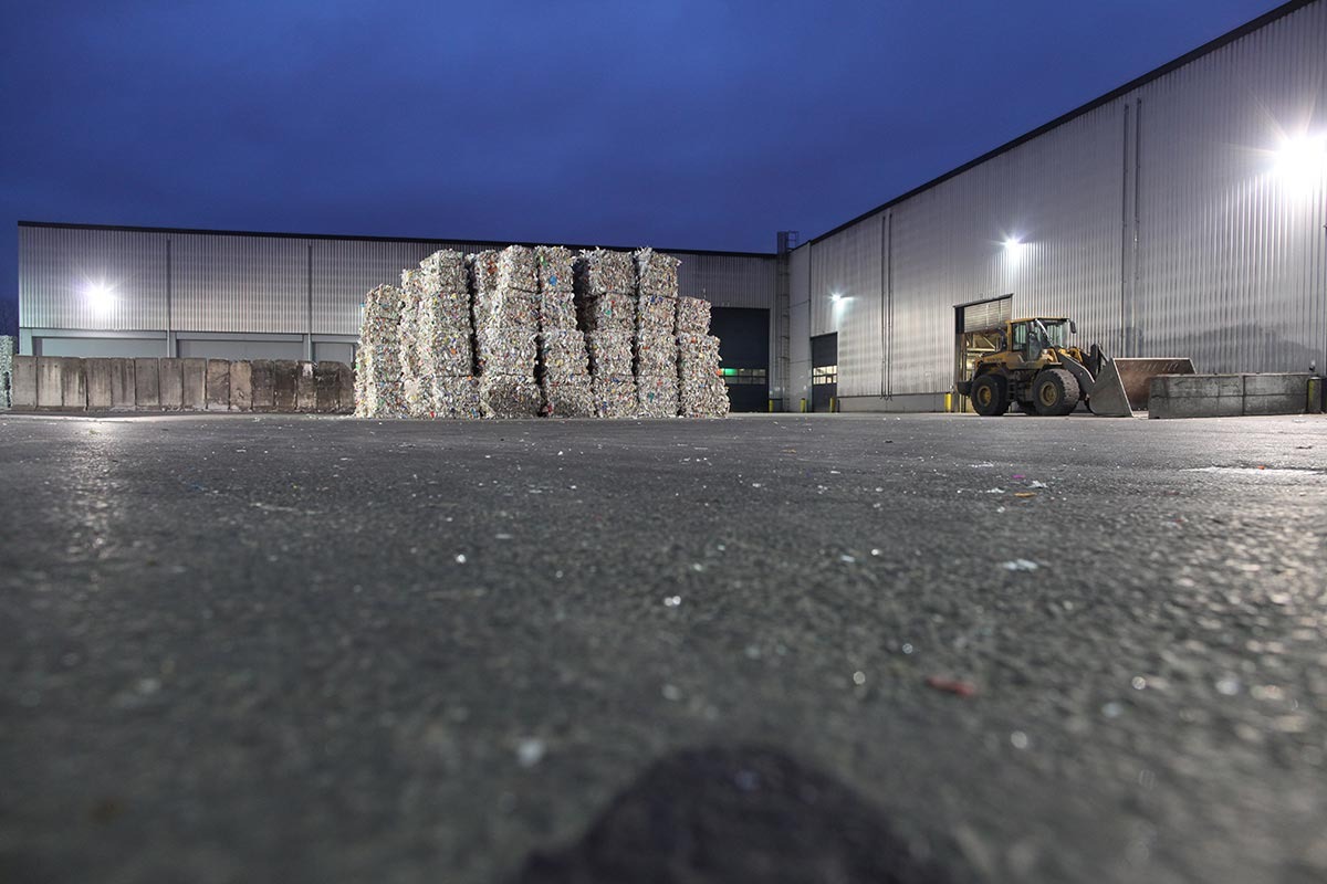 Quadratische Plastik-Müllballen stehen vor einer Halle.