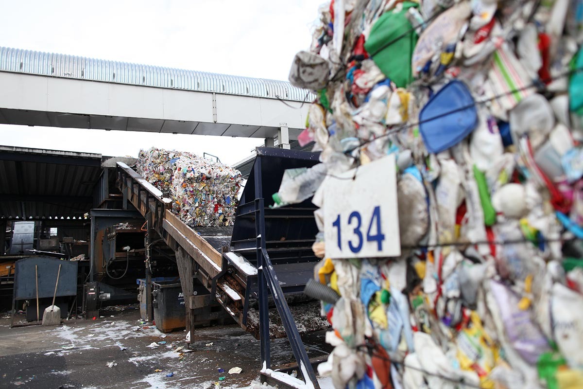 Plastikmüllballen laufen draußen auf ein überdachtes Förderband.