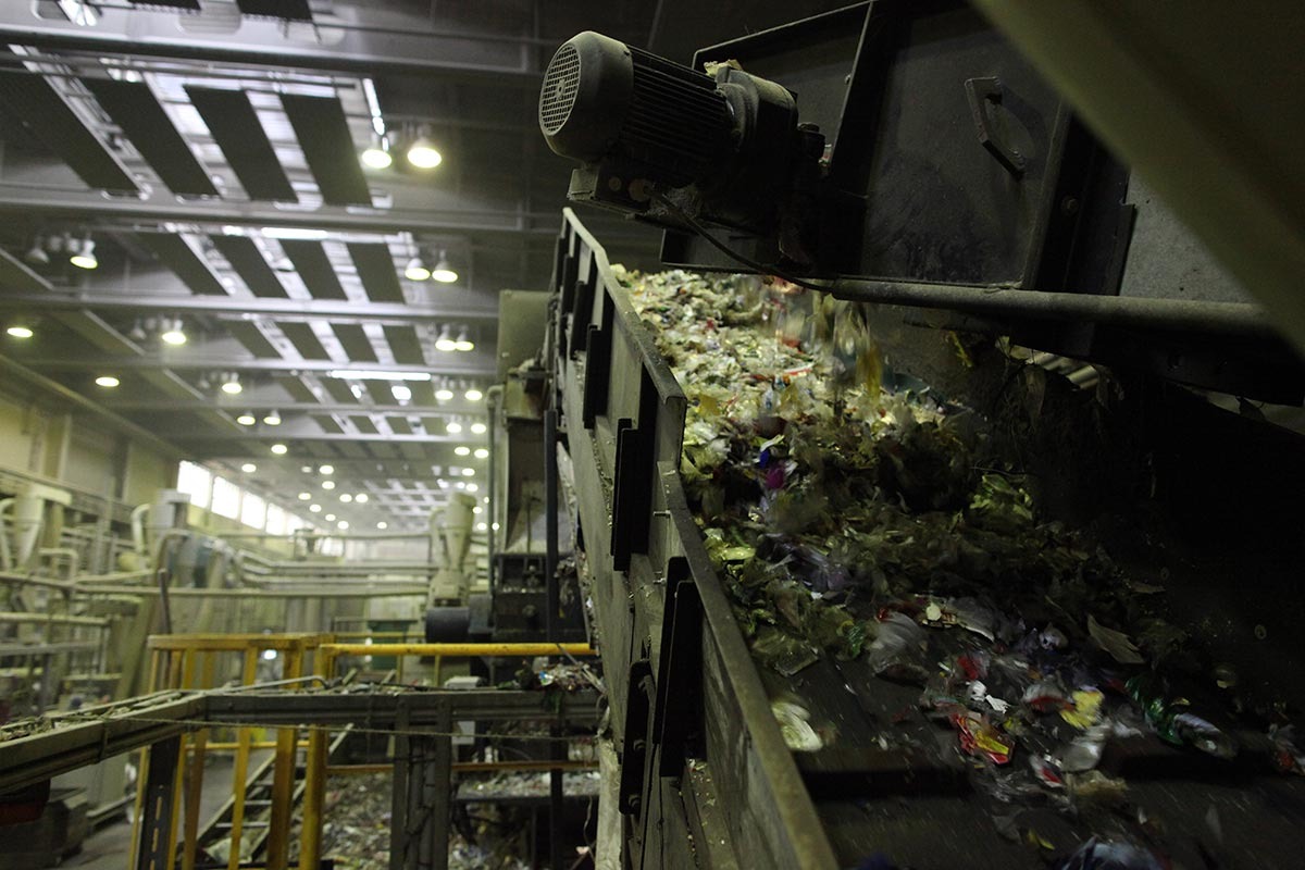 Plastikmüll läuft in eine Halle auf ein Förderband.