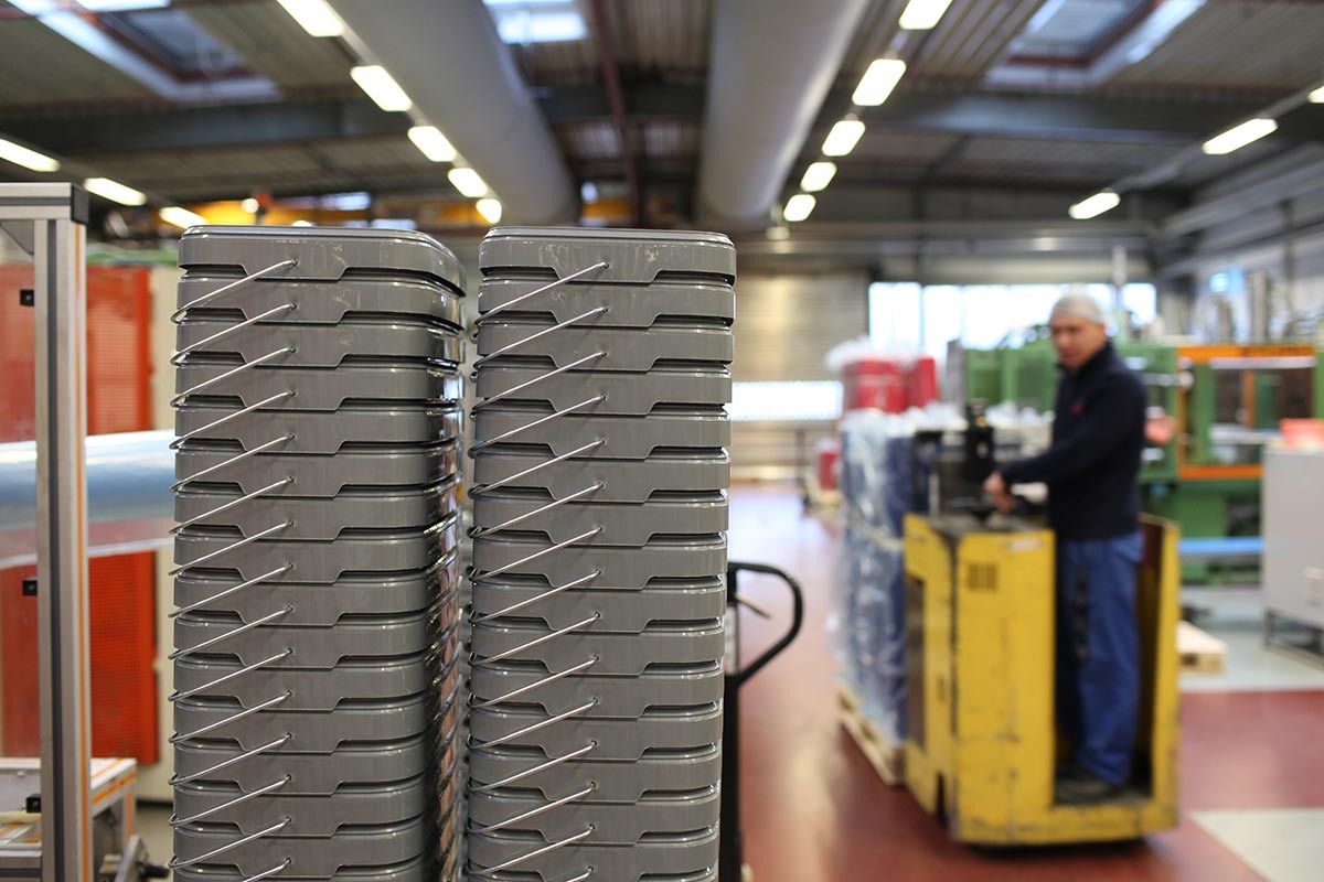 : Ineinander gestapelte graue recycelte Plastikeimer in einer Fertigungshalle.