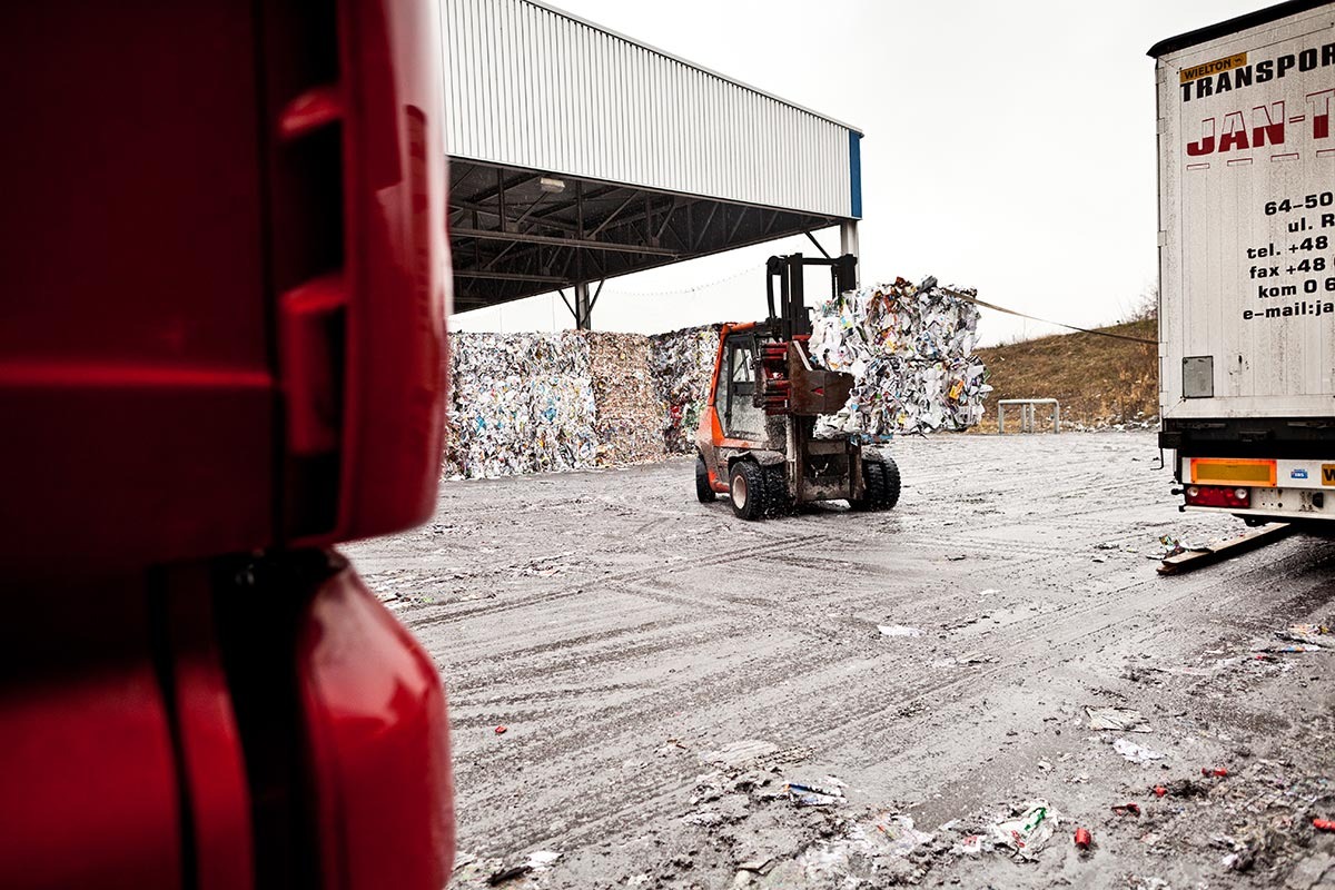 Gabelstapler transportiert quadratisch gepressten Altpapierballen von einer Außenlagerhalle zu einem LKW.