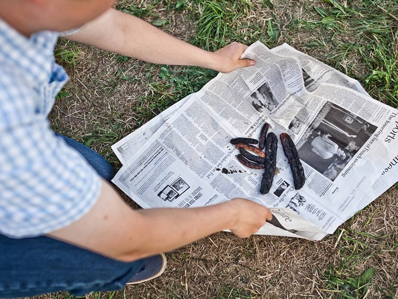 Ein Mann schlägt verkohlte Grillwürstchen in Zeitungspapier ein.