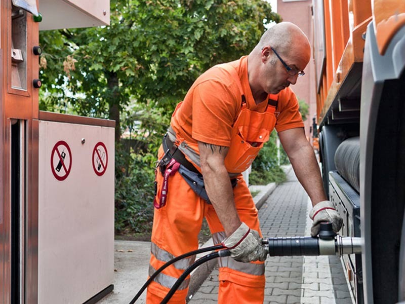 Ein Mann in oranger Arbeitskleidung befüllt den Tank eines Müllfahrzeuges.