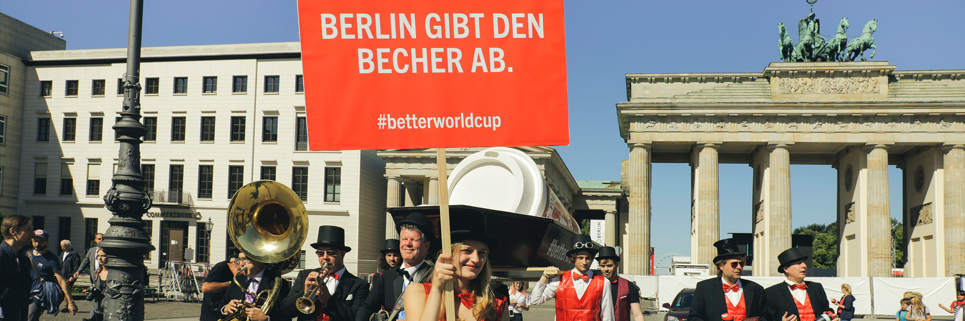 Gruppe von Menschen ist festlich gekleidet, hält ein Schild hoch vor dem Brandenburger Tor in Berlin