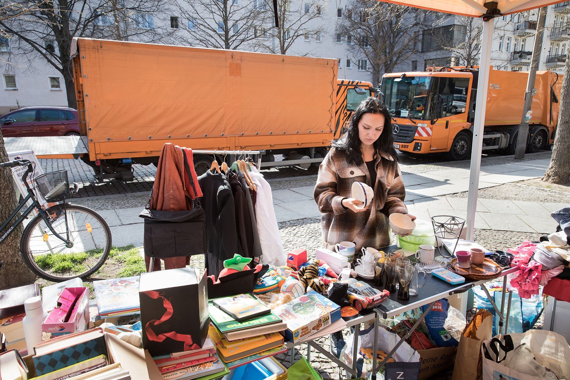 Klimawoche 2025 in Steglitz-Zehlendorf: Eine junge Frau steht an einem Verkaufsstand, wo es Second Hand-Artikel zu kaufen gibt.